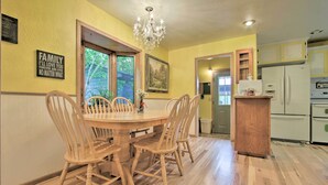 Un comedor con una mesa y sillas de madera, un candelabro y una cocina con electrodomésticos blancos.