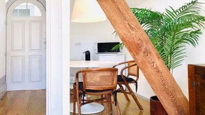 Ett rum med en vit dörr, ett matbord med två stolar, en lampa, en tv och en krukväxt.