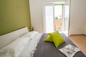 A bedroom with a bed, a green pillow, a tray with glasses and a cup, and a view through a sliding door.