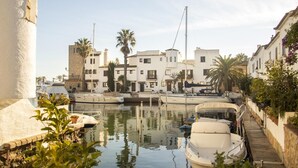 A marina with boats docked, white buildings, and palm trees.