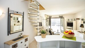 A modern living room with a white staircase, a large mirror, a TV, and a fruit bowl on a white table.
