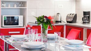 A modern kitchen with red cabinets, a white microwave, a coffee maker, and a glass table set for dining.