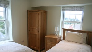 Une chambre avec deux lits simples, une armoire en bois, une table de chevet avec une lampe et des fenêtres avec des rideaux.
