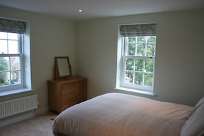 A bedroom with a bed, a dresser, and two windows with curtains.