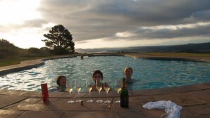 Une piscine où trois personnes se détendent, tenant des verres à vin et une bouteille.