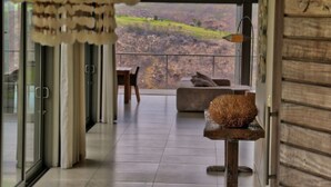 Un intérieur moderne avec une grande porte vitrée donnant sur un balcon qui offre une vue sur un paysage vallonné.