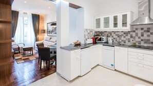 A modern kitchen with white cabinets, a dishwasher, and a microwave. There is a dining area with a table and chairs, and a living room with a sofa and a coffee table. - PUERTA DEL SOL CITY CENTER III WITH BALCONY (Madrid)