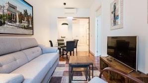 A modern living room with a grey sofa, a TV, and a dining area with a table and chairs. - PUERTA DEL SOL CITY CENTER III WITH BALCONY (Madrid)