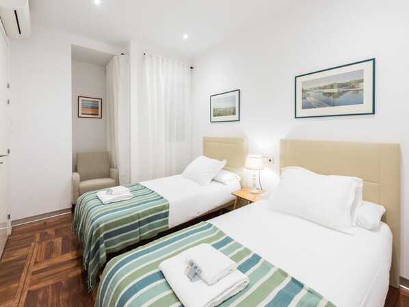 A hotel room with two beds, a chair, a nightstand, and a picture on the wall.