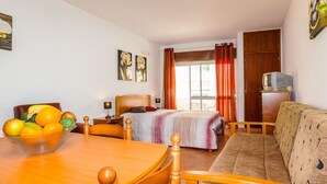 Une chambre d’hôtel avec un lit en bois, un canapé, une table à manger avec des fruits et un téléviseur posé sur un meuble.