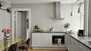 A modern kitchen with white cabinets, a wooden countertop, and a built-in oven. There are two pendant lights, a vase with flowers, and a plant on the counter.