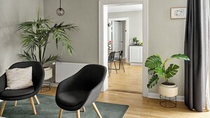 A modern living room with two black chairs, a potted plant, and a view into the dining area.