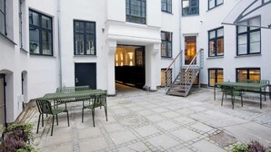 A courtyard with a staircase leading to an upper floor, outdoor seating area with tables and chairs, and a building entrance with a black door.