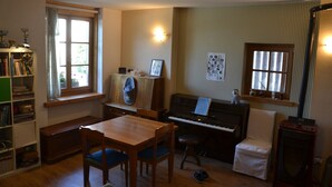 Een gezellige woonkamer met een piano, een eettafel en een boekenkast.