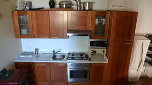 Een kleine keuken met houten kastjes, een RVS fornuis en een koelkast.