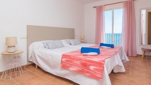 Ein Hotelzimmer mit einem Bett, zwei Nachttischen, einem Fenster mit Vorhängen und Blick aufs Meer.