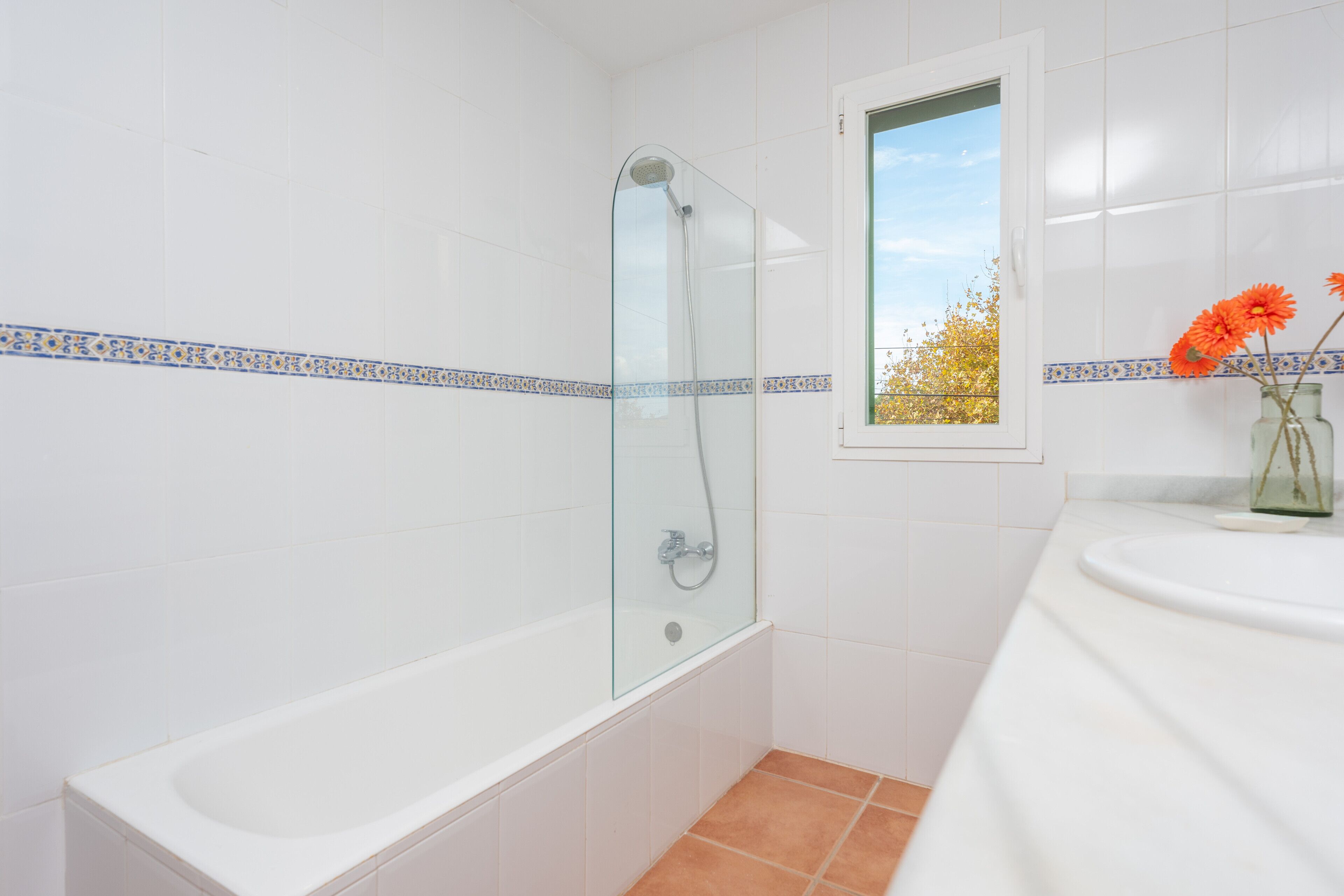 Une salle de bain dotée d’une douche à parois de verre, d’une baignoire blanche et d’une fenêtre donnant sur la verdure.