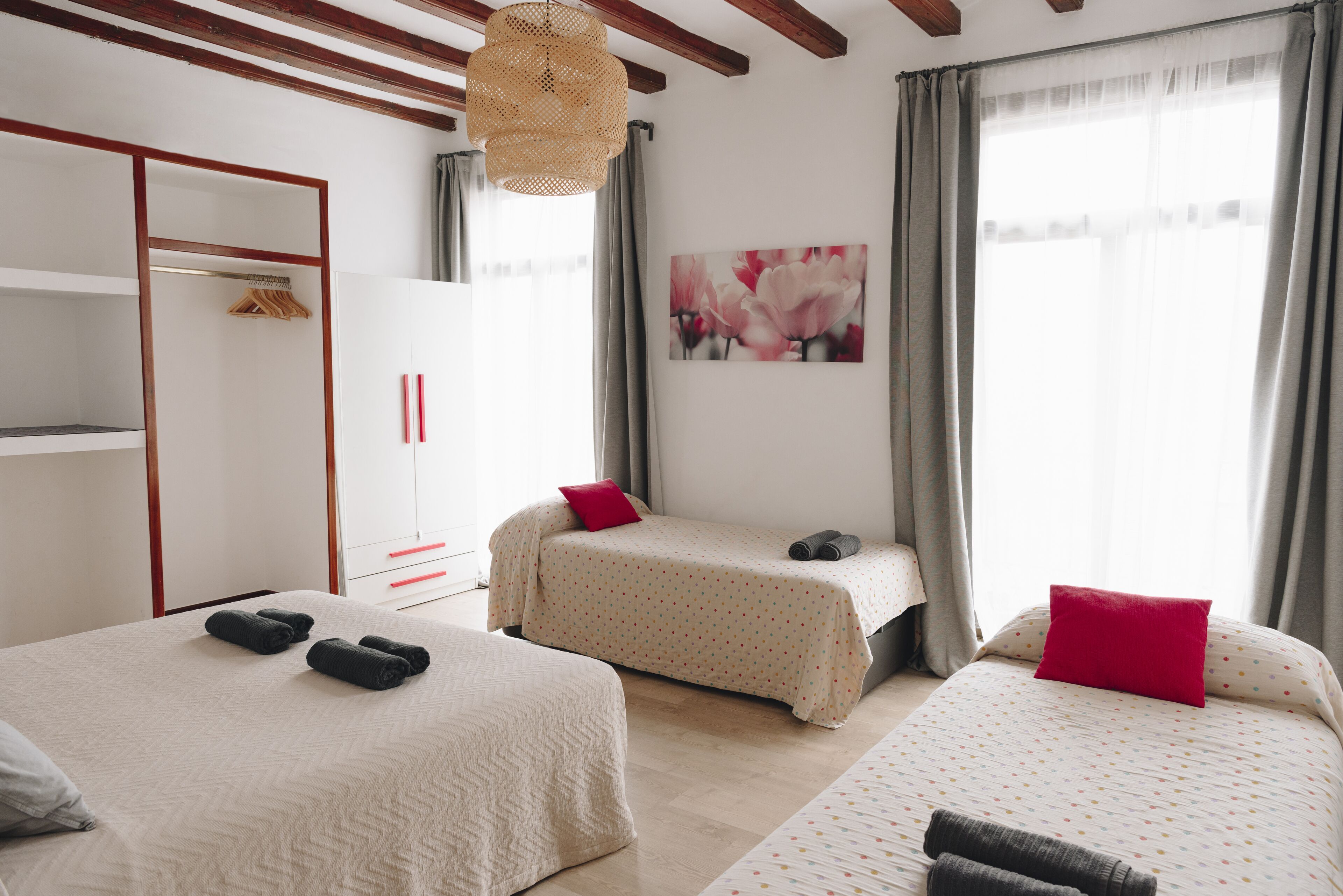 A hotel room with two beds, a wardrobe, a painting, and a window with curtains.