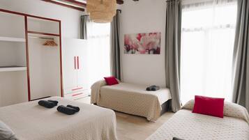 A hotel room with two beds, a wardrobe, a painting, and a window with curtains.