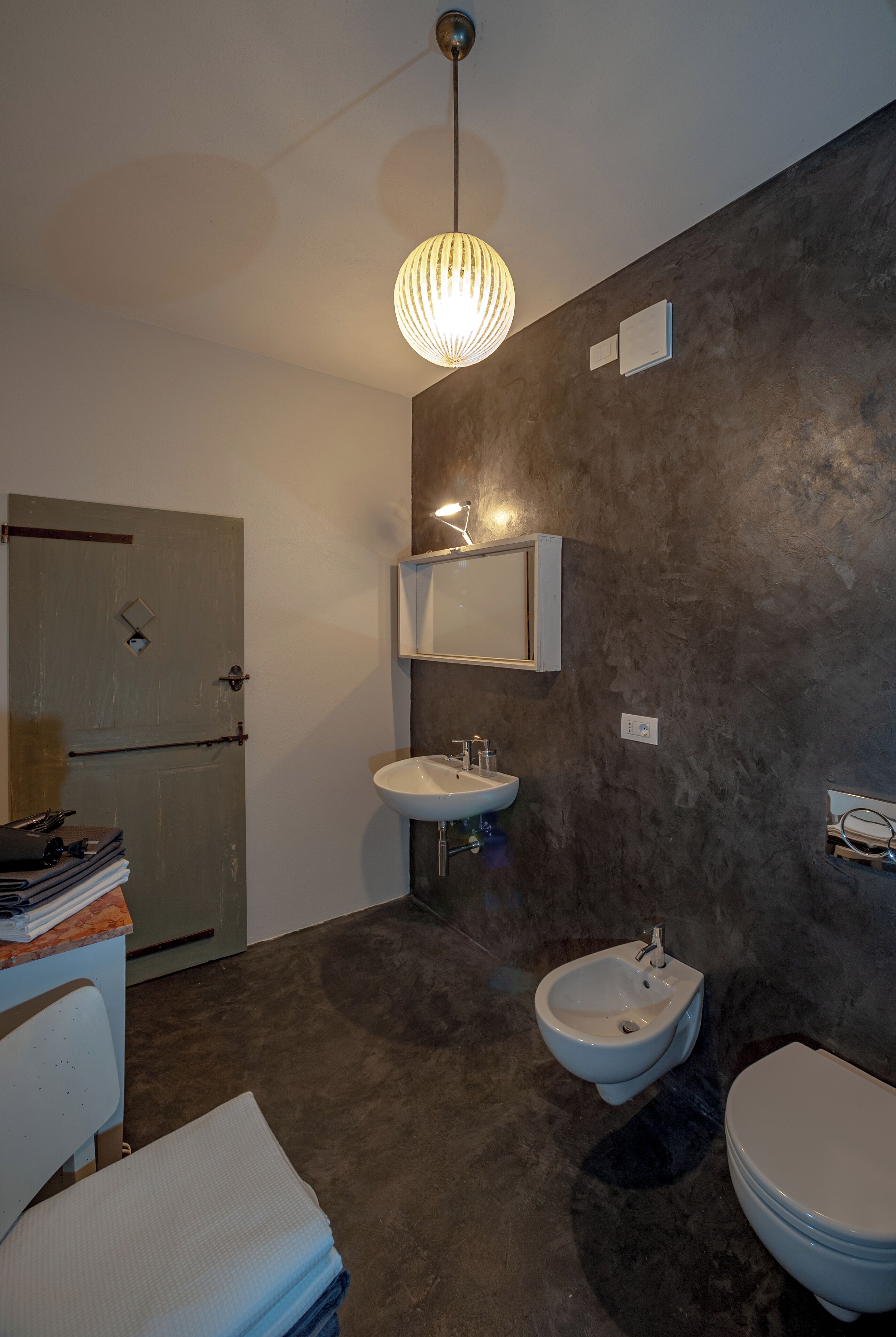 A modern bathroom with a dark textured wall, a white sink, a bidet, and a toilet.