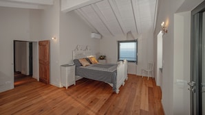 A bedroom with a wooden floor, a bed with a patterned bedspread, a nightstand, a window with a view, and a door. - NEW! Villa beautiful sea view, facing PORTOFINO, 30 minutes from the FIVE EARTHS (CHIAVARI)