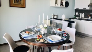 Ein Essbereich mit einem runden Tisch, gedeckt für vier Personen, umgeben von weißen Stühlen. Auf dem Tisch steht eine weiße Vase mit Blumen und Kerzen.