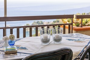 A table with two glass vases containing candles and decorative items, set against a scenic view. - Little Sunshine apartment (Taormina)