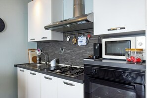 A modern kitchen with a gas stove, a microwave, and a stainless steel range hood. - Little Sunshine apartment (Taormina)