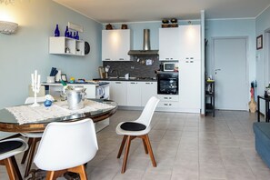 A modern kitchen with white cabinets, a dining table with chairs, and a microwave. - Little Sunshine apartment (Taormina)