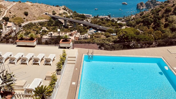 Ein Pool auf dem Dach mit Liegestühlen, Blick auf das Meer und eine Brücke im Hintergrund.