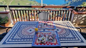 Ein Balkon mit einem mit Fliesen belegten Tisch, gedeckt für zwei Personen, mit einer dekorativen Tischläufer und einem kleinen Teller mit Speisen.
