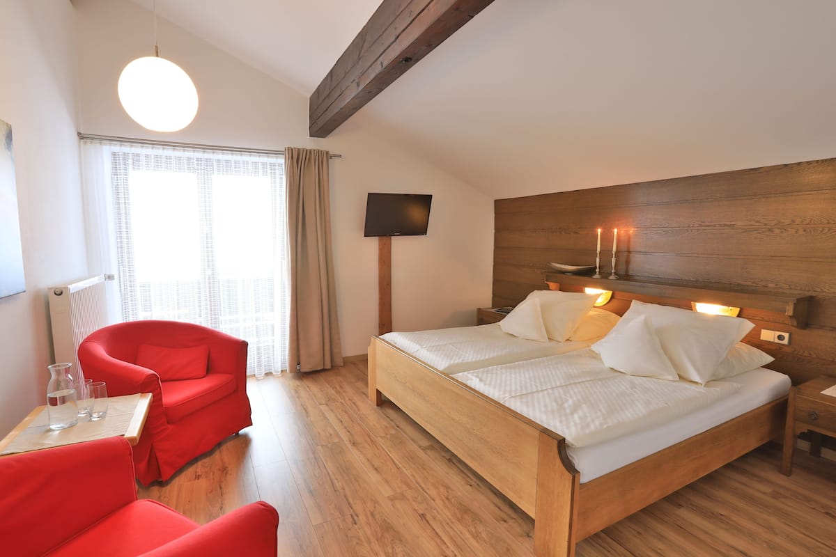 A bedroom with a wooden bed, a red chair, a bedside table, and a TV mounted on the wall.