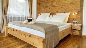 A wooden bed with a headboard, a bedside table, and a window with curtains. - Gästehaus Wiesegg (Reit im Winkl)