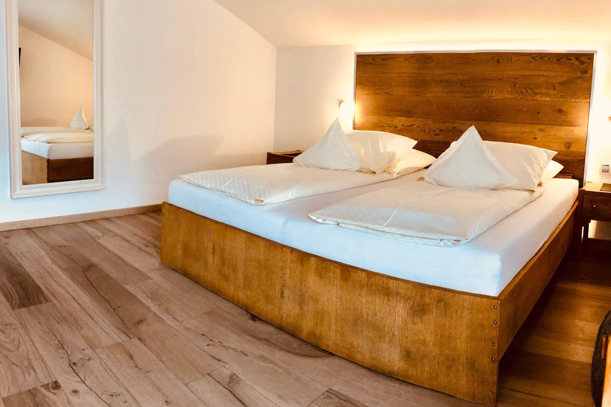 A modern bedroom with a wooden headboard, a large mirror, and a wooden floor.