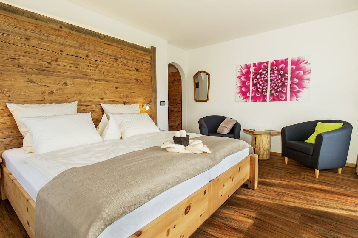 A bedroom with a wooden headboard, a large bed with white linens, a blue armchair, and a small wooden side table.