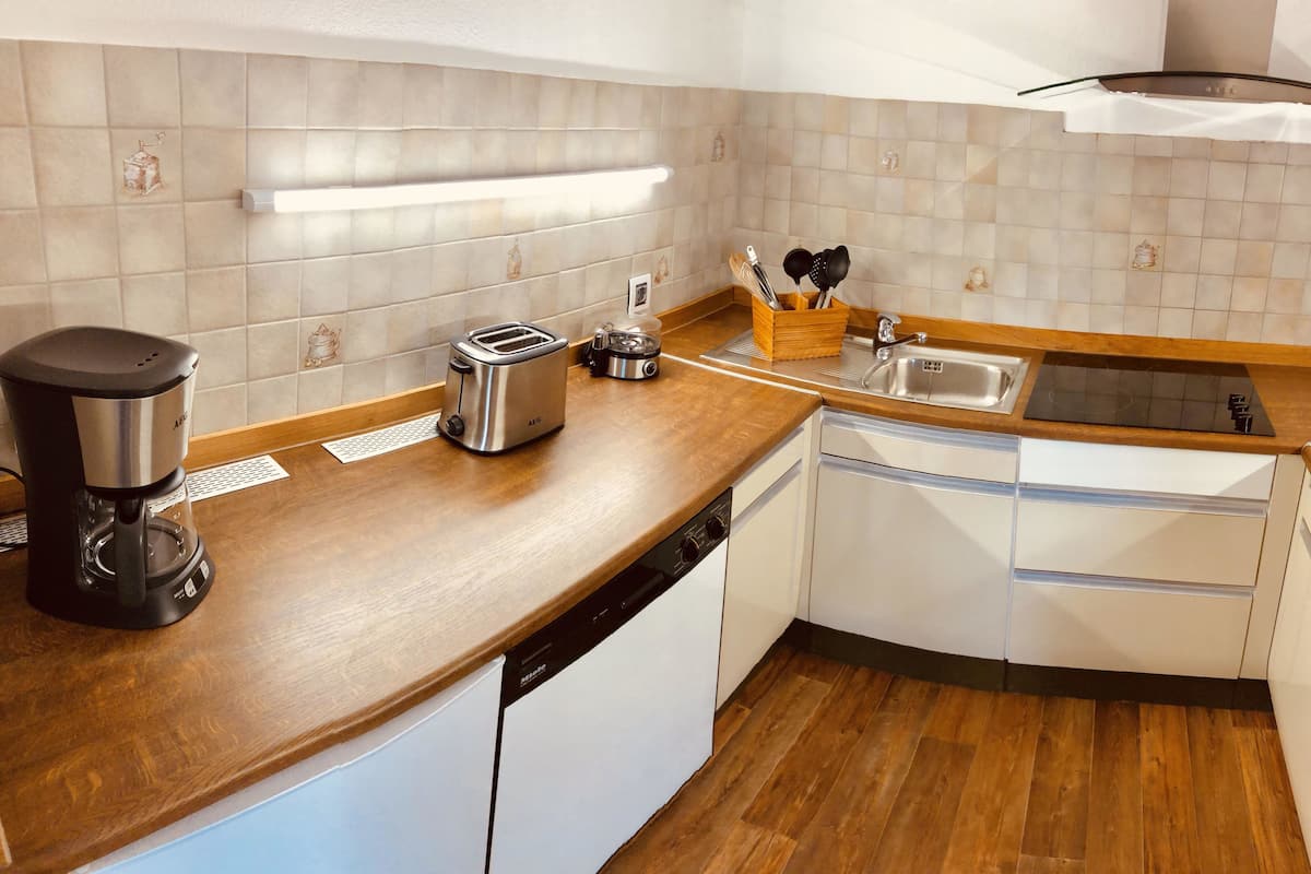 A modern kitchen with a dishwasher, a coffee maker, a toaster, and a sink.