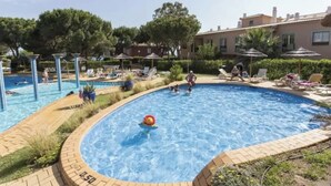 A swimming pool with lounge chairs and umbrellas, surrounded by greenery and buildings. - Amazing Duplex w/ Stunning Pool by HostWise (Albufeira)