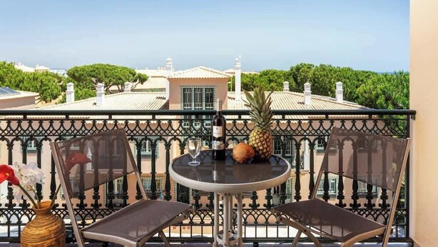 A balcony with two chairs, a table, a bottle of wine, and a pineapple. - Amazing Duplex w/ Stunning Pool by HostWise (Albufeira)