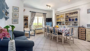 A dining area with a table set for four, a blue sofa, and a television in the background. - Amazing Duplex w/ Stunning Pool by HostWise (Albufeira)