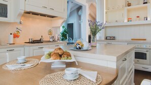 A kitchen with white cabinets, a wooden island with breakfast items, and a view into the dining area. - VILLA LILLA penthouse on the beach of San Vincenzo Tuscany luxury (San Vincenzo)