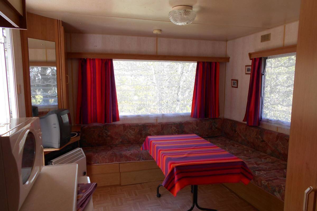 Interior compacto de autocaravana con cama sofá, una mesita, microondas y ventana con cortinas rojas.