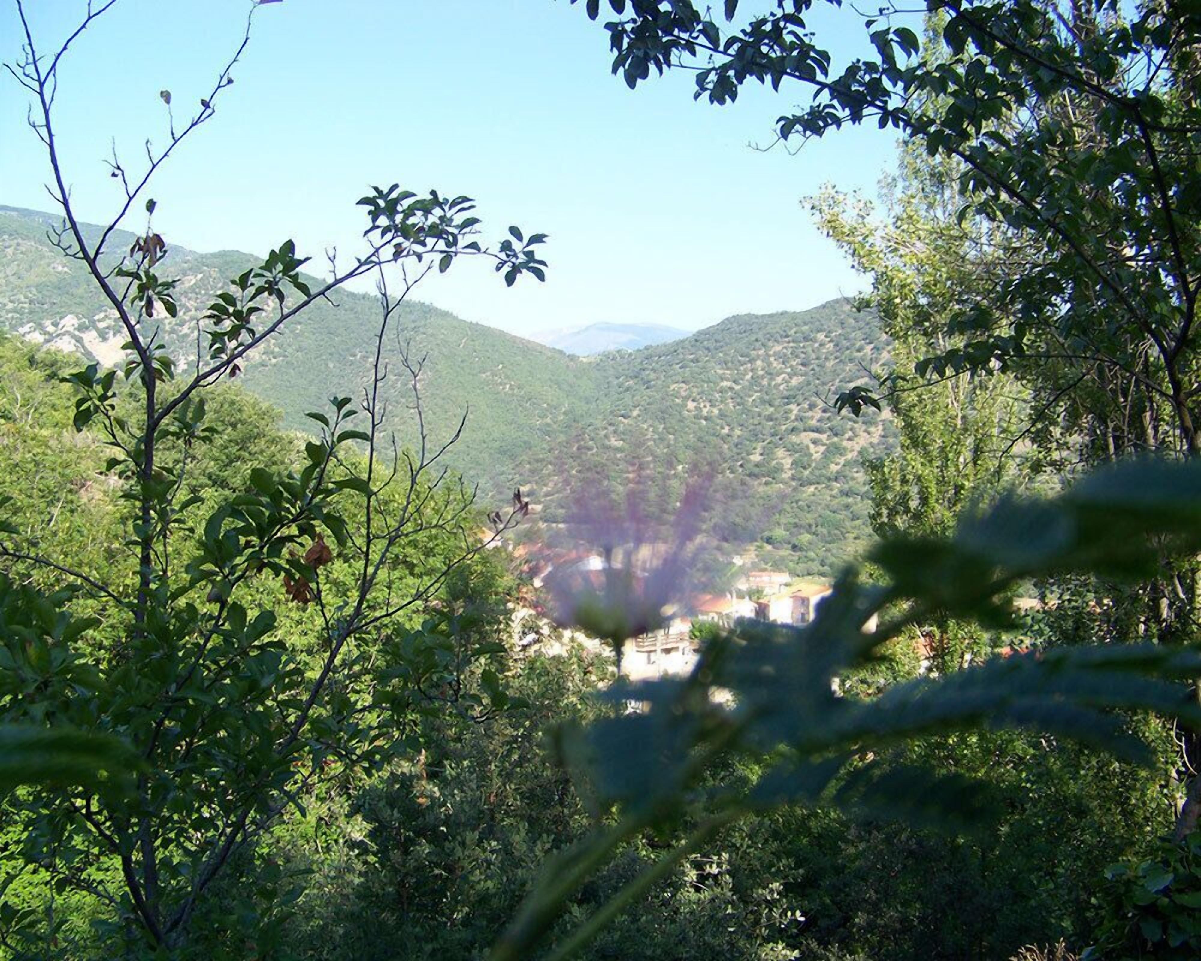A view of a valley with a building in the distance, surrounded by dense greenery and hills.
