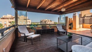Eine Holzterrasse mit Sitzgelegenheiten im Freien, einem Fernseher und Blick auf Gebäude in der Ferne.