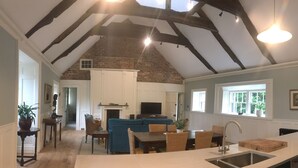A spacious living area with a high ceiling, exposed beams, a fireplace, a television, and a dining area with wicker furniture. - Number 6 Narrow Water Castle (Warrenpoint)