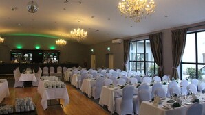 Un salón de banquetes con mesas dispuestas para un evento formal, con candelabros y ventanas amplias.