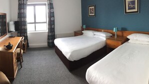 Una habitación de hotel con cama, escritorio, silla, televisor y ventana con cortinas.