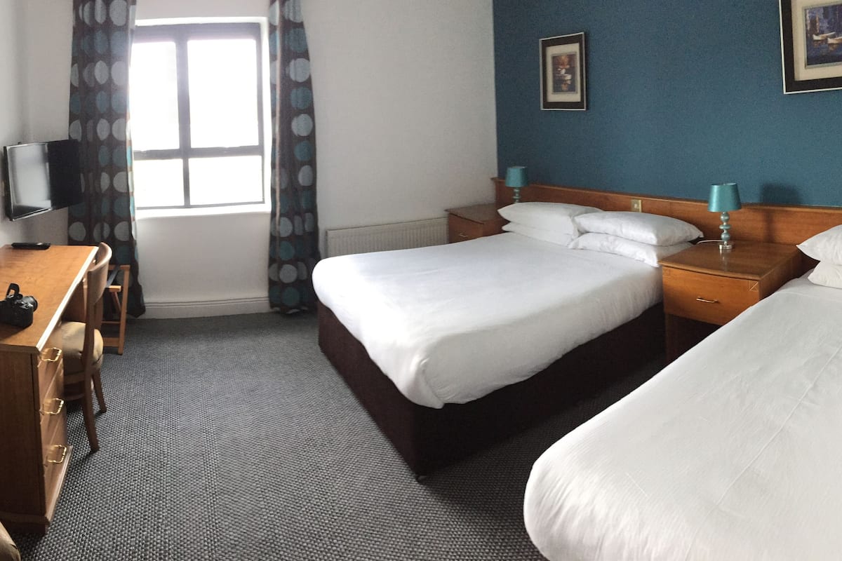 A hotel room with a bed, a desk, a chair, a television, and a window with curtains.
