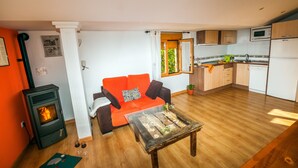 Un espace de vie compact comprenant un canapé, une table basse en verre, un poêle à bois, un coin cuisine avec des placards et un four à micro-ondes, ainsi qu’une fenêtre avec des rideaux.