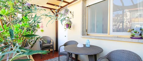 Un patio con mobiliario de mimbre, una mesa redonda y plantas en macetas.