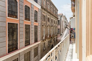A narrow urban street with multi-story buildings, balconies, and a pedestrian walkway.